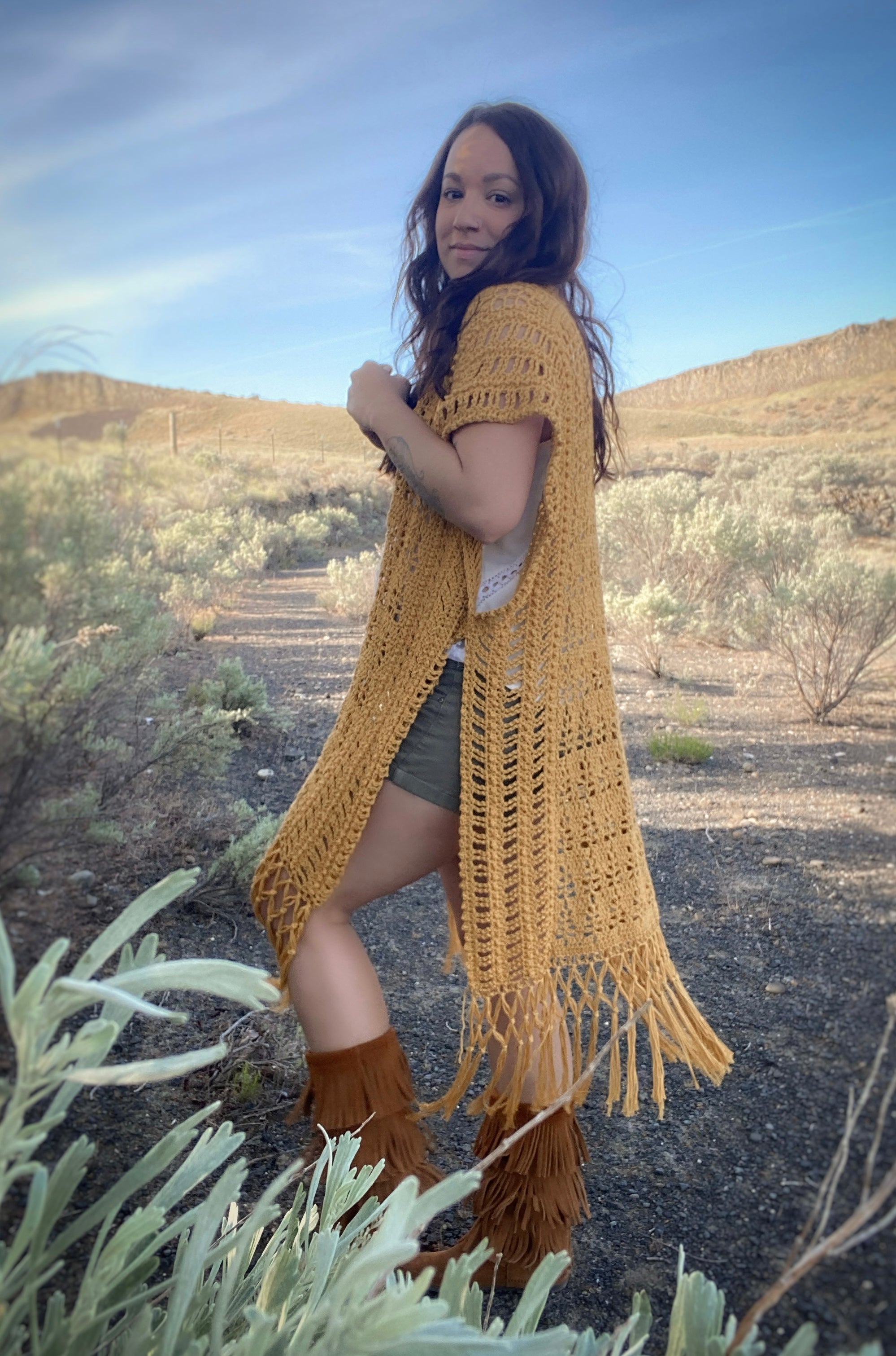 Woman wearing a yellow crochet cardigan with fringes in a desert landscape