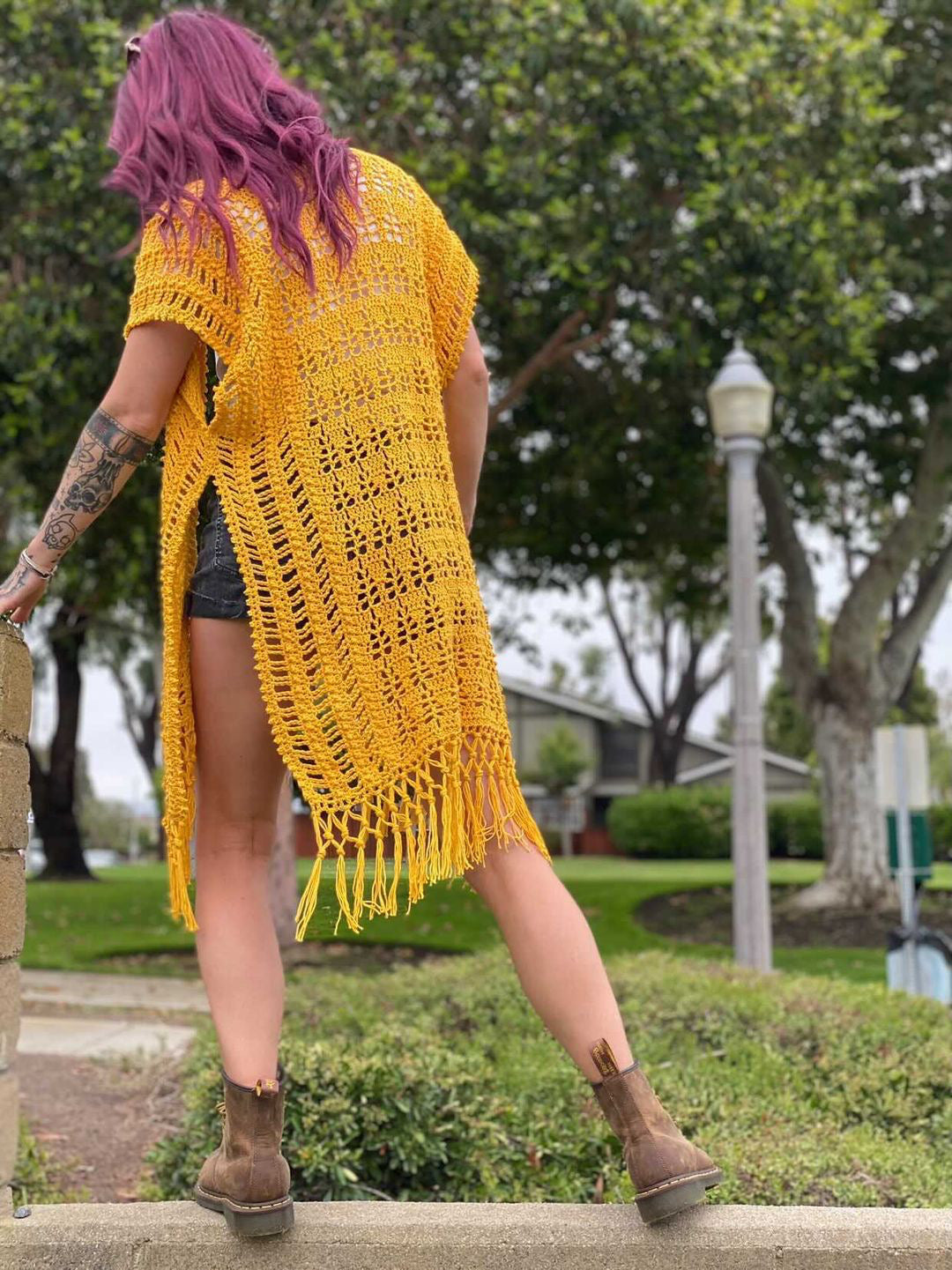 Person wearing a yellow crochet poncho with fringe in an outdoor setting