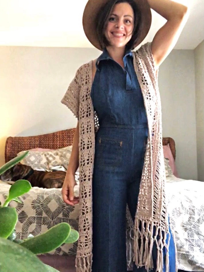 Woman wearing a denim jumpsuit with a beige cardigan in a bedroom setting