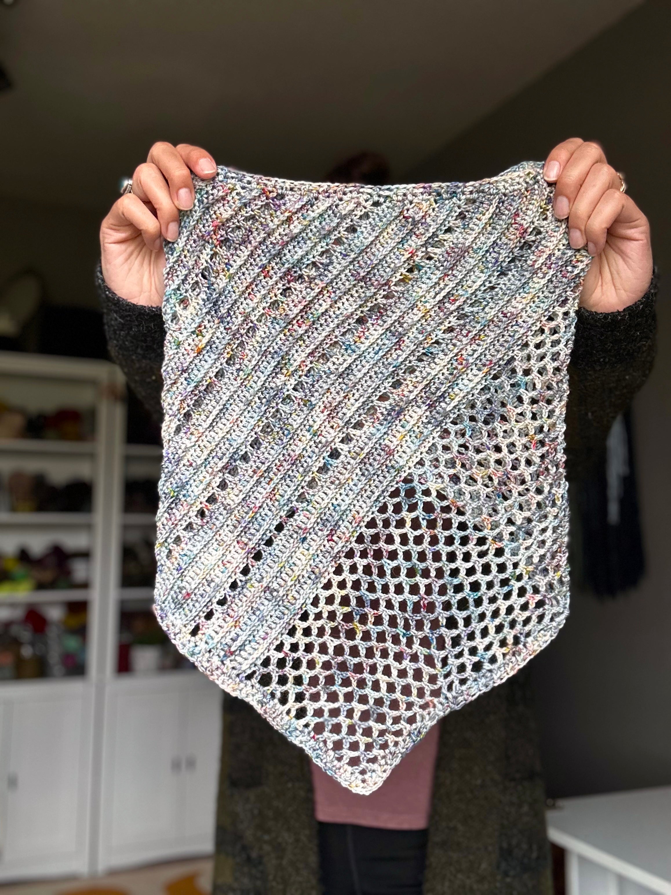 Person holding a multicolored crochet bandana scarf in a home setting