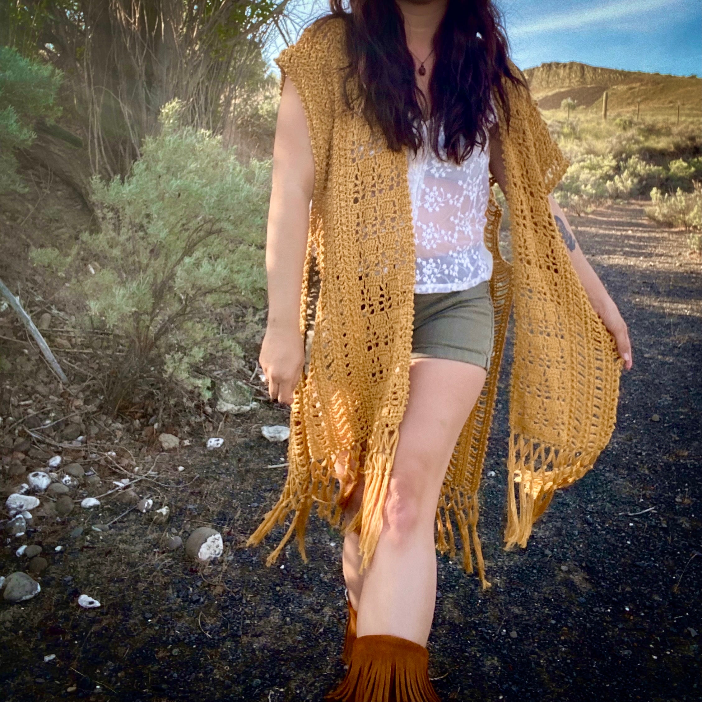 Person wearing a mustard yellow crochet cardigan in a desert setting