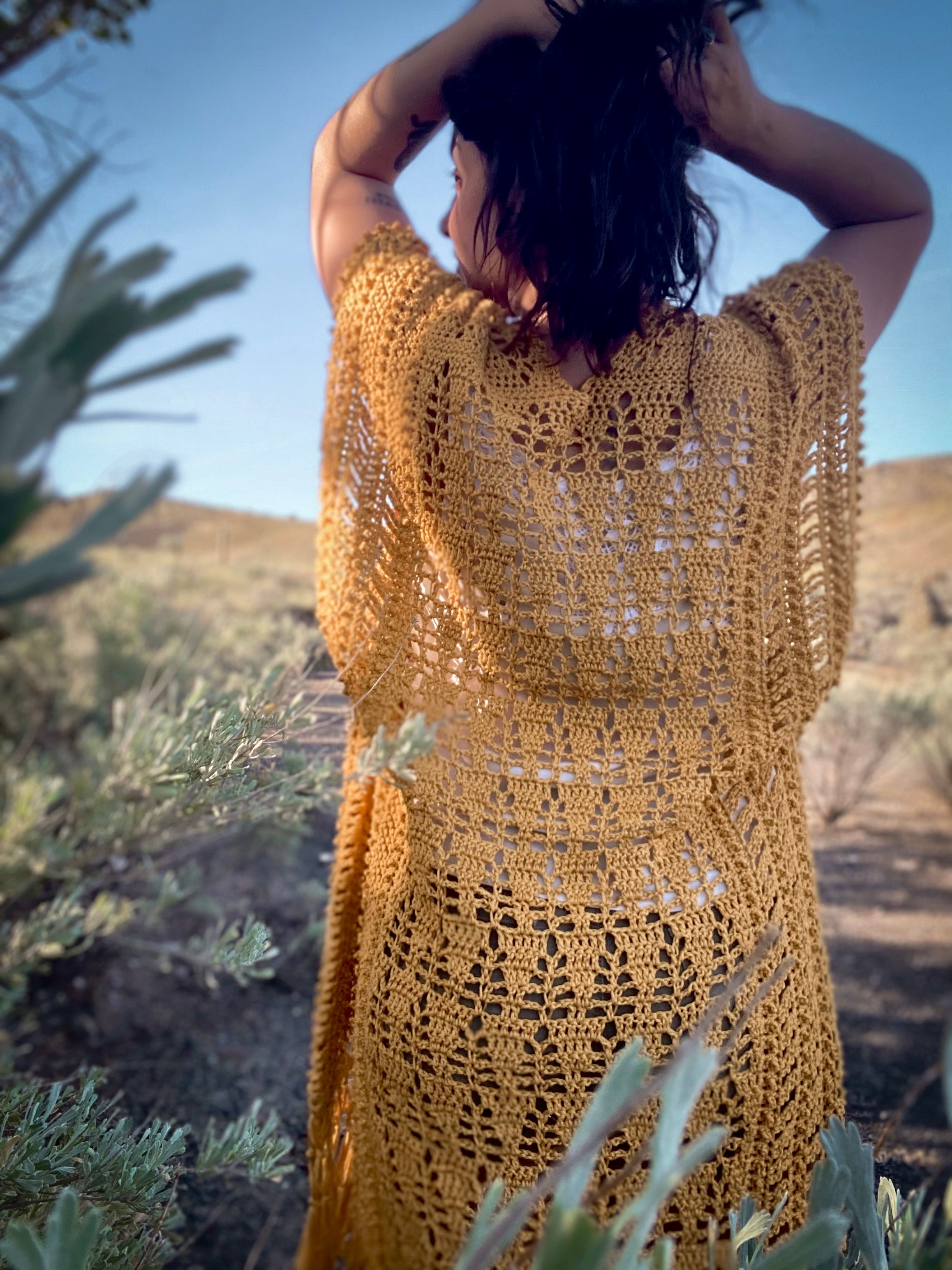 Woman wearing a yellow crochet dress standing outdoors with greenery around