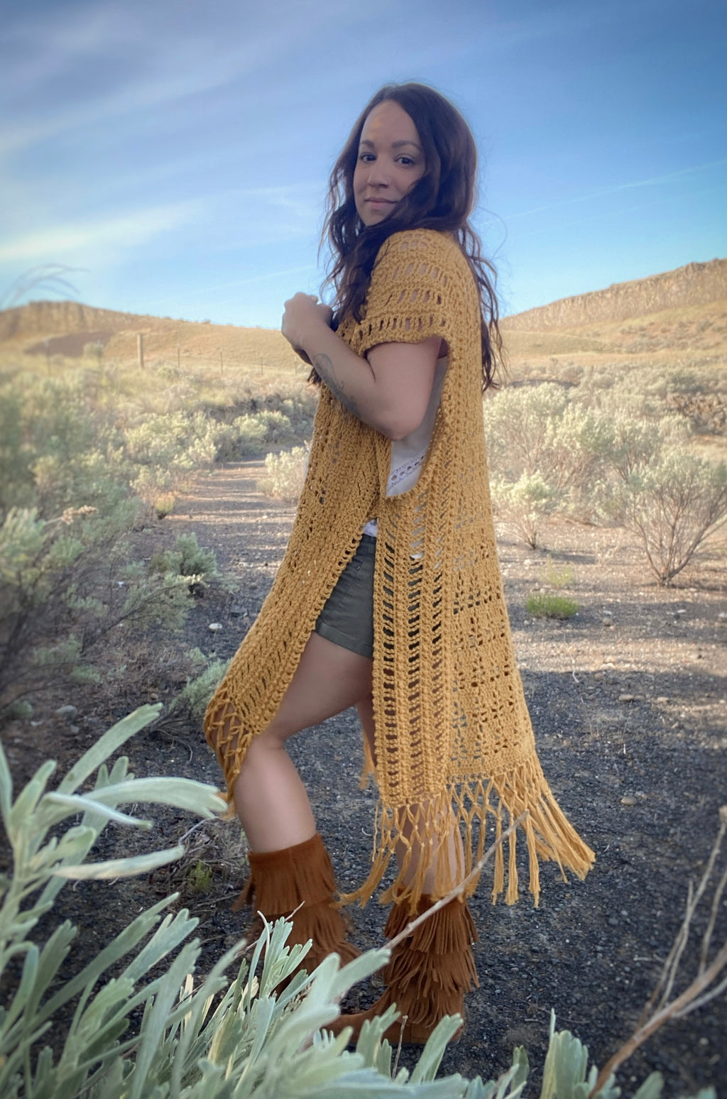 Woman wearing a yellow crochet cardigan with fringes in a desert landscape